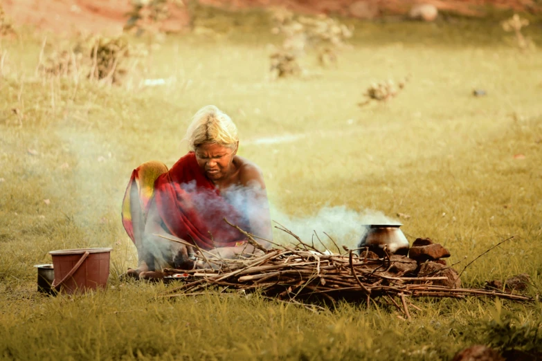 a woman sitting on a field while cooking food