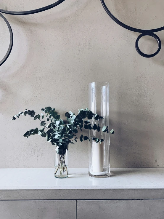 two clear vases filled with greenery sitting on a table