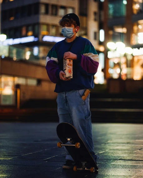 a boy stands with his skateboard in front of him while wearing a face mask