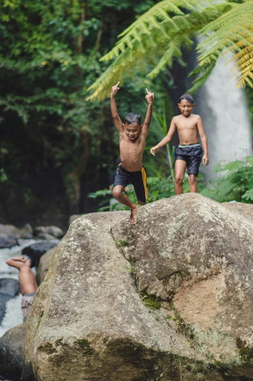 three s jumping from rocks in front of a waterfall