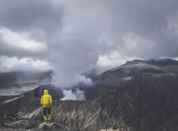 a man wearing a yellow jacket standing on a mountain peak