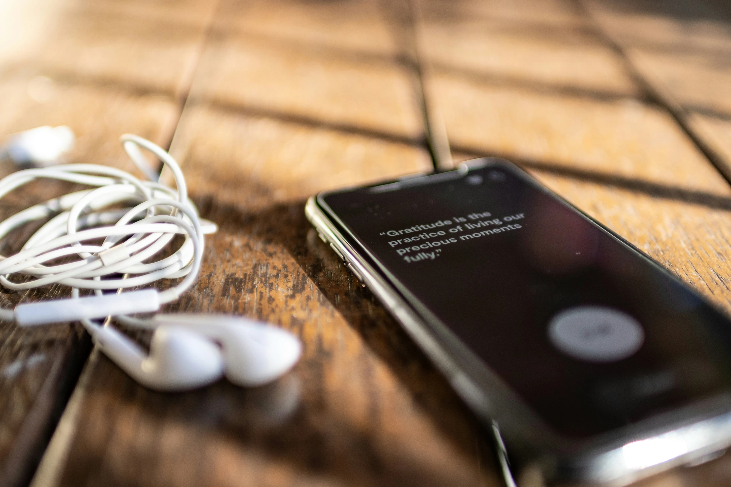 a smart phone hooked up to earphones on top of a wooden table