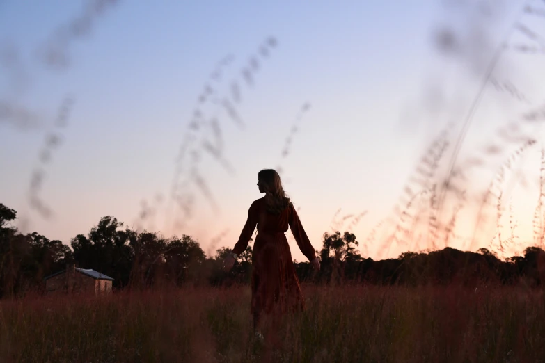 a woman is walking through a field at sunset
