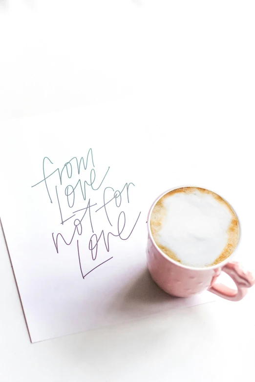 a pink mug sitting on top of a table next to a note