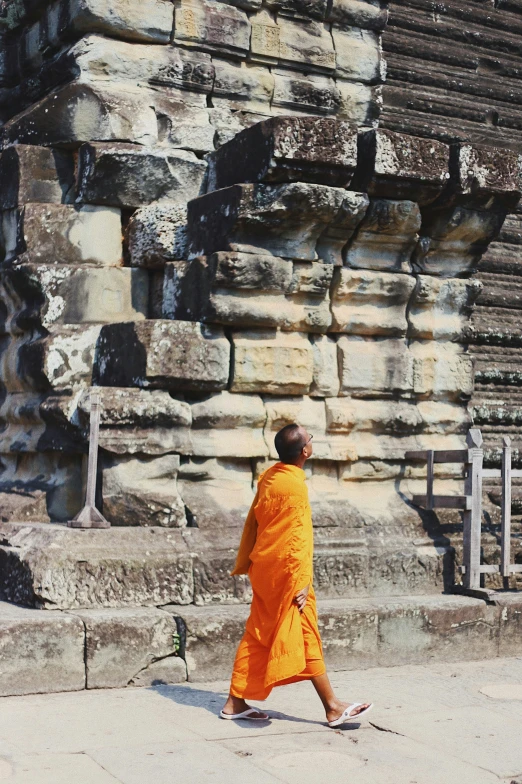 a monk walks on the ground next to an old stone wall