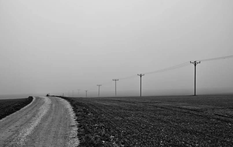 a dirt road with power lines on it and an empty field in the foreground