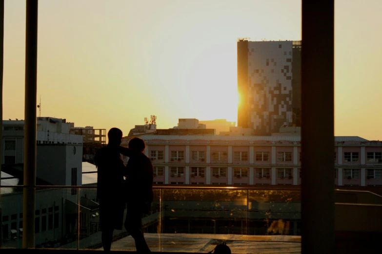 a couple stand on a balcony as the sun sets