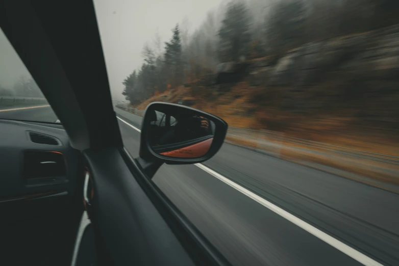 a side view mirror reflecting trees on the side of a road