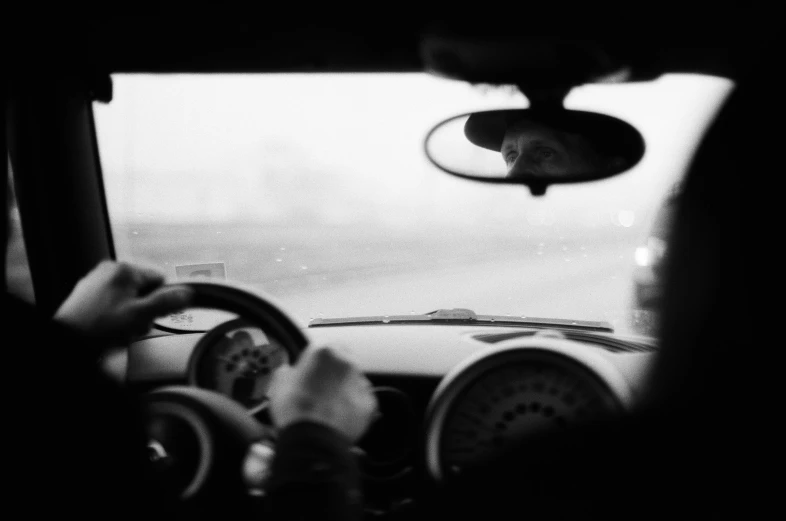 a man driving his car with a dog sitting in the drivers seat