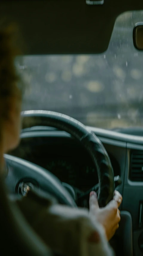 a woman driving a car in the rain while holding the steering wheel