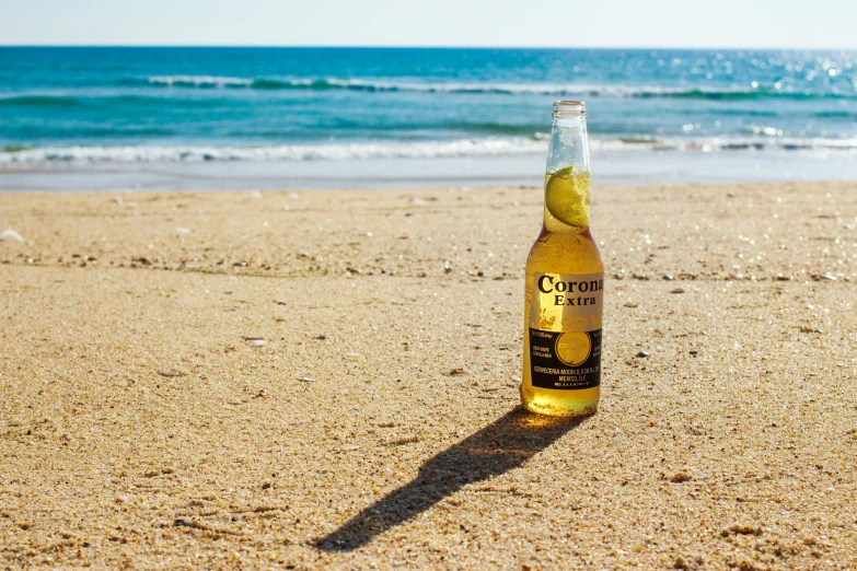 a glass bottle of beer sitting in the sand