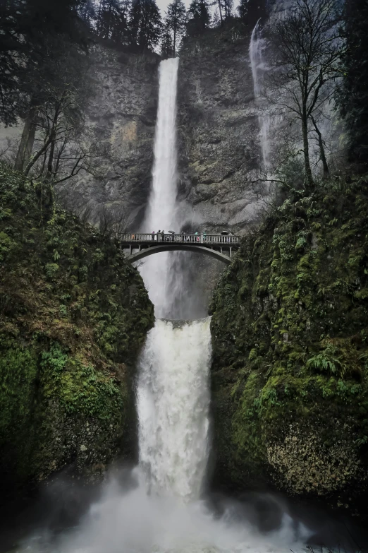 a waterfall with a bridge and people on the edge