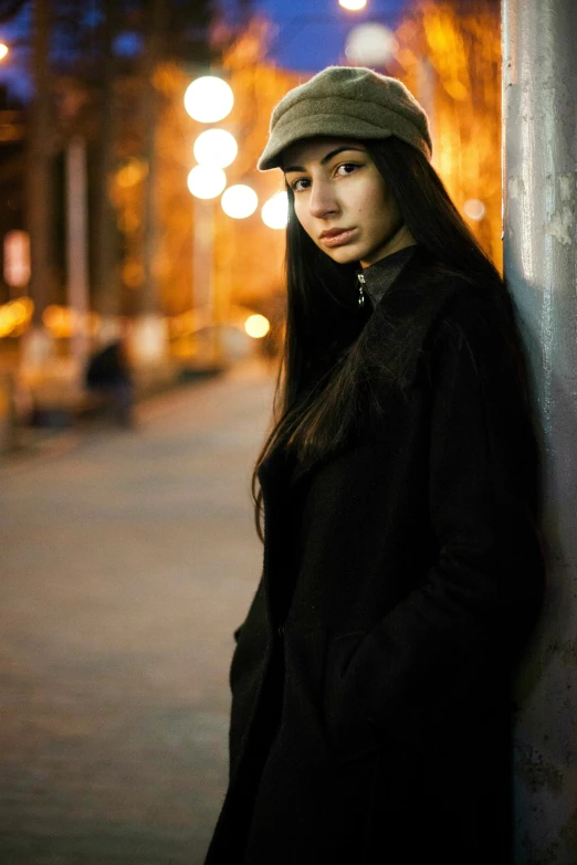 a girl leaning up against a pole with a cap on