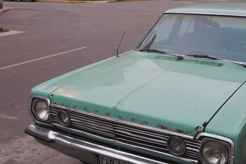 the old green car is parked next to the curb