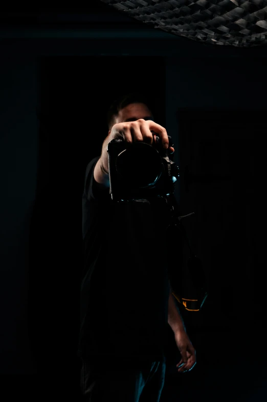 man holding camera in dark room by black curtain