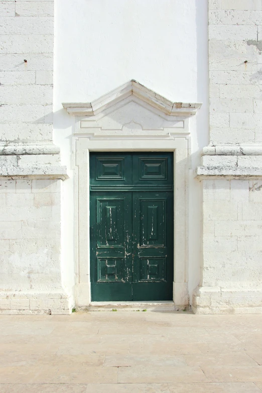 a green door on a white building that has a small clock on the front of it