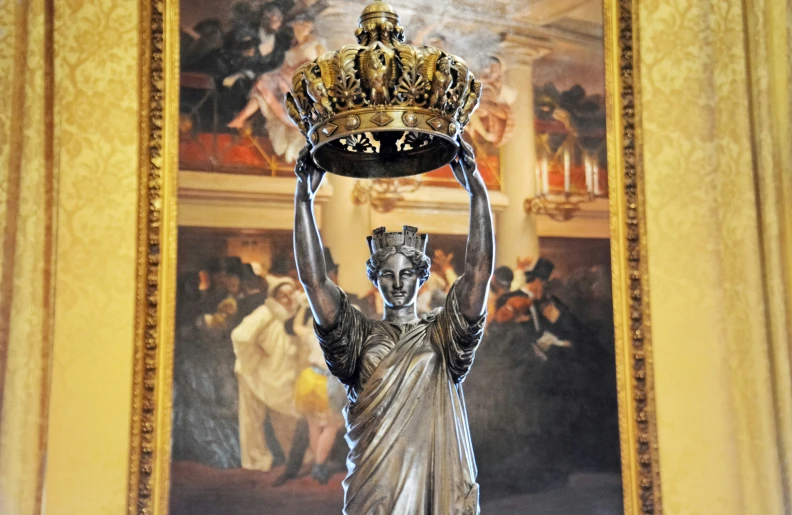 a statue that is holding a large object in front of a painting