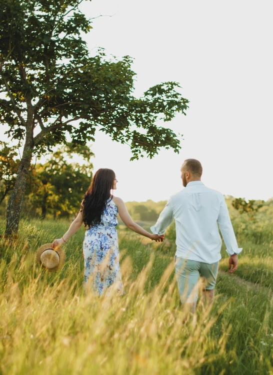 a man and woman walking hand in hand through tall grass holding hands