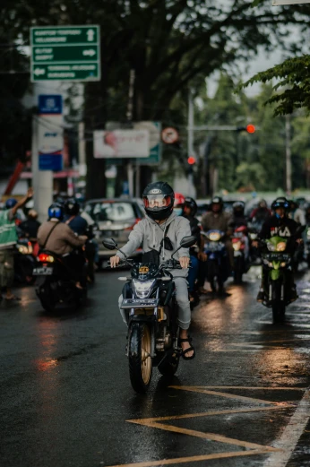 some people riding motorcycles down a street in the rain