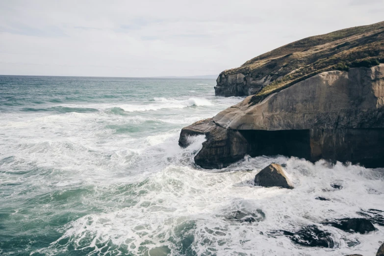 an ocean area with rocks, waves and a hill