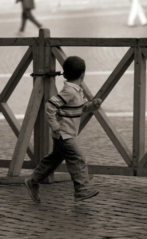 a little boy holding onto a fence while walking