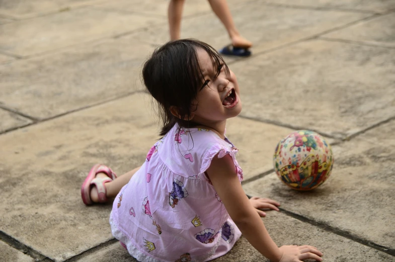 a little girl sitting on the ground playing with a ball