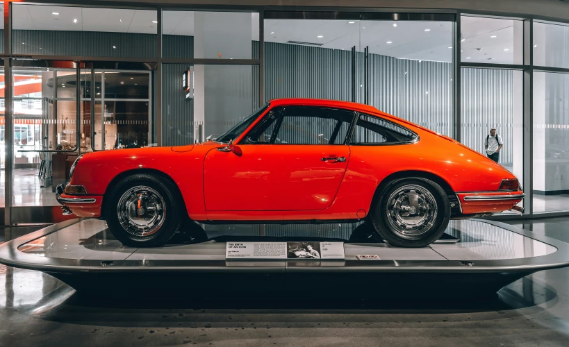 a shiny orange classic car on display at a museum