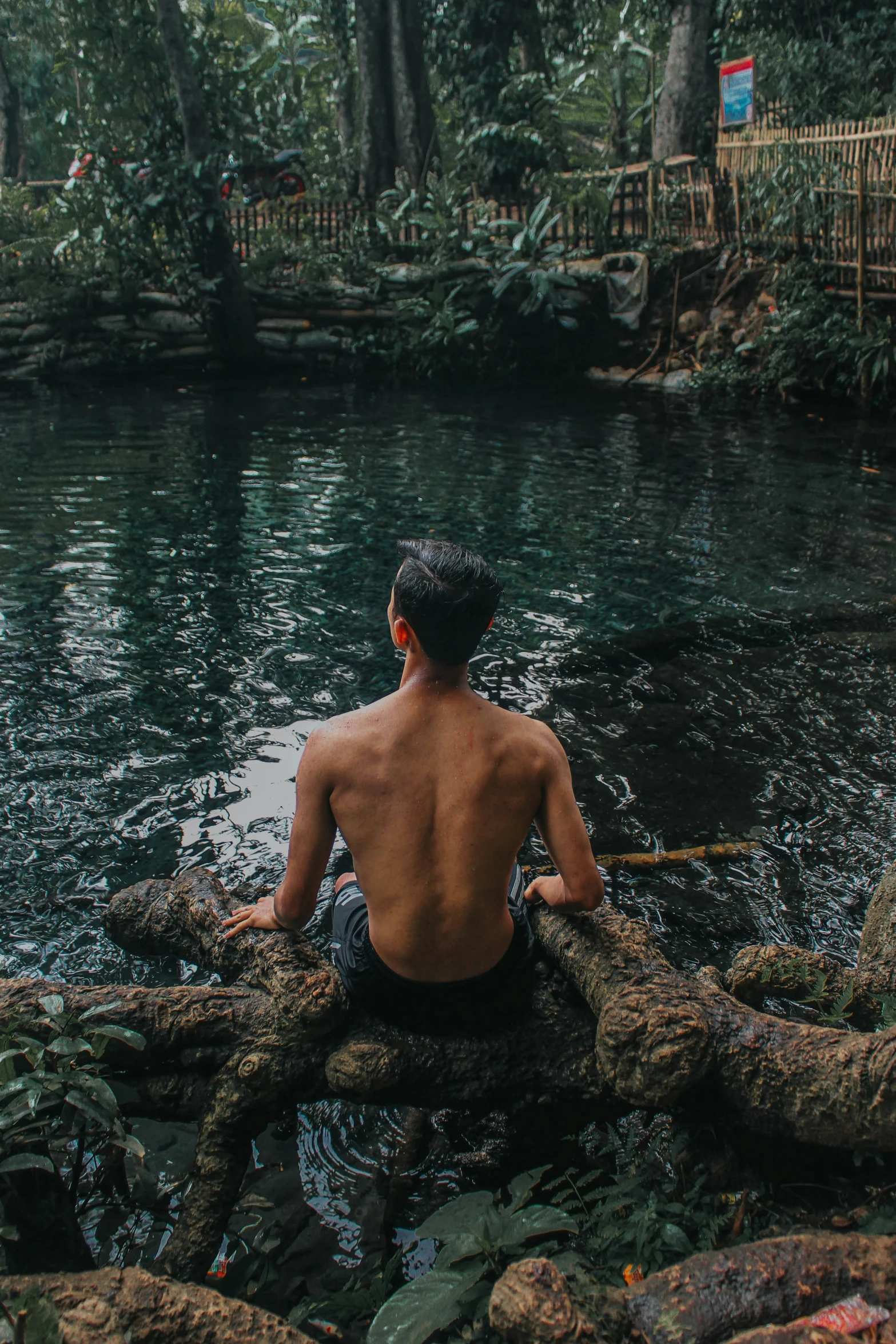 a person sits on the rocks in a body of water with a pole and boat