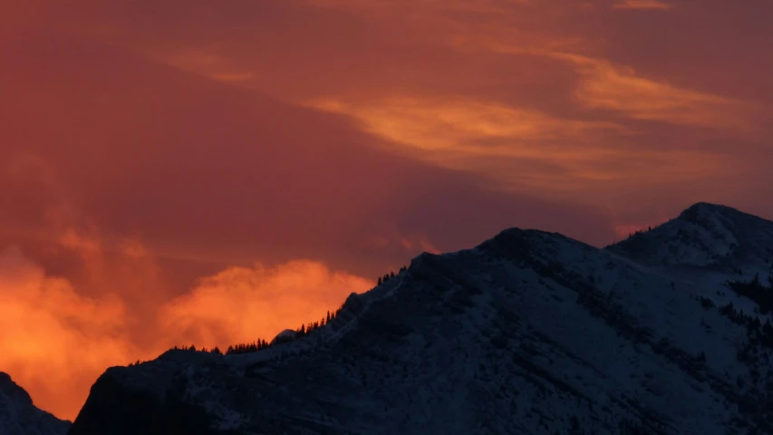 a skiier with his ski poles stuck in the air, riding high up a mountain with an orange glow on top of it