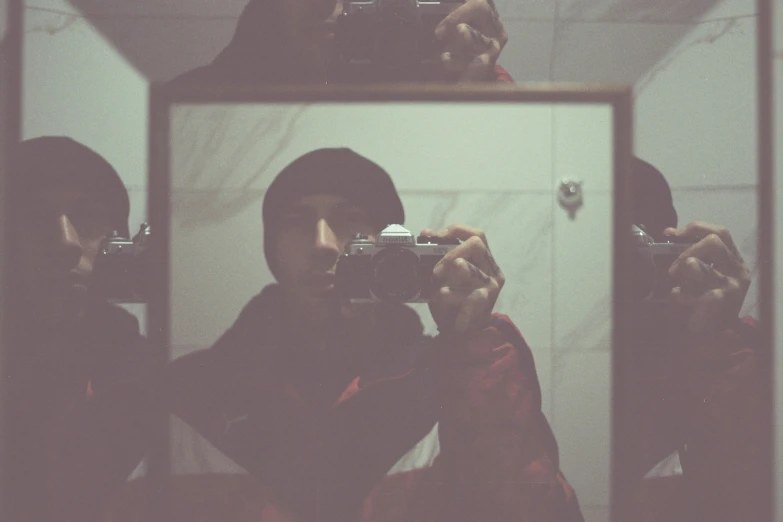 a man holding up a camera looking at himself in the mirror