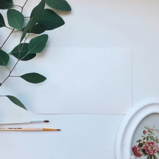 some pink flowers and leaves sitting next to an empty white paper on a white surface