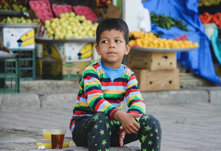 a  sits on the ground near a fruit stand