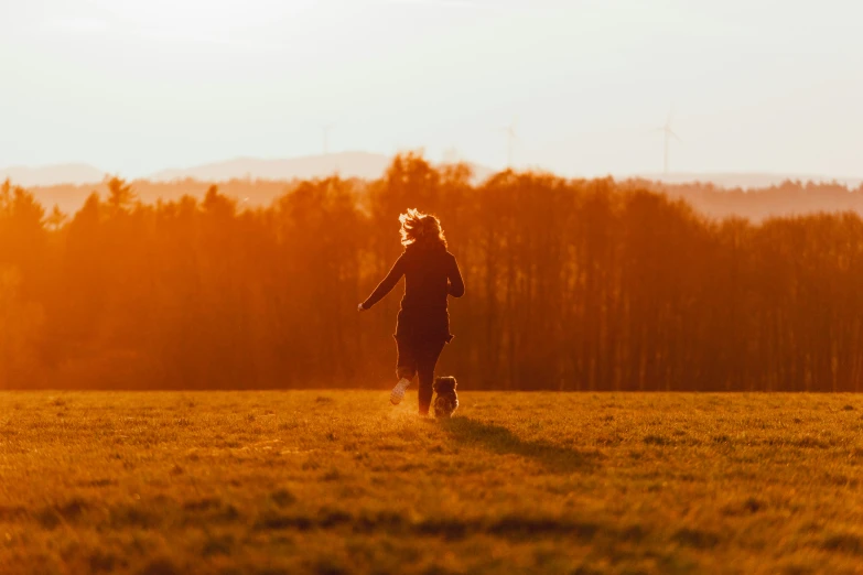 a woman walks through a field with trees in the background