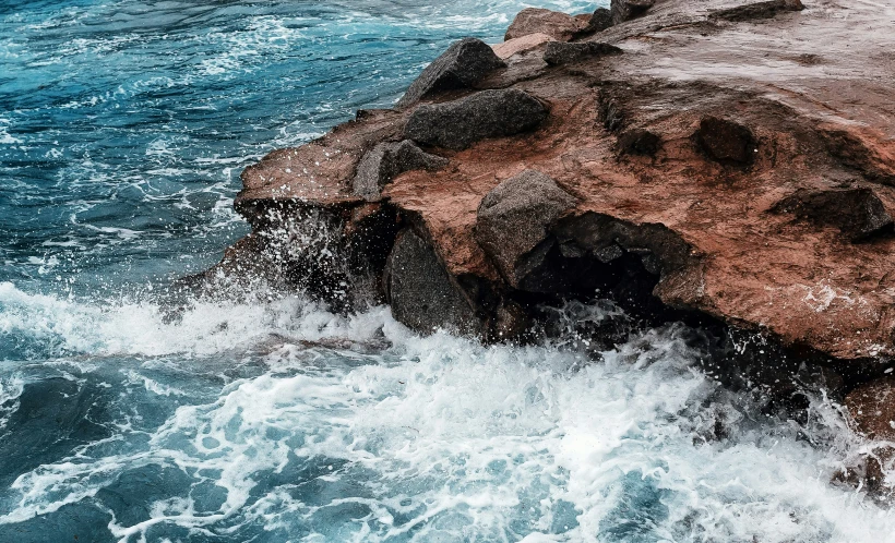 an elephant walking across water next to a rocky coast