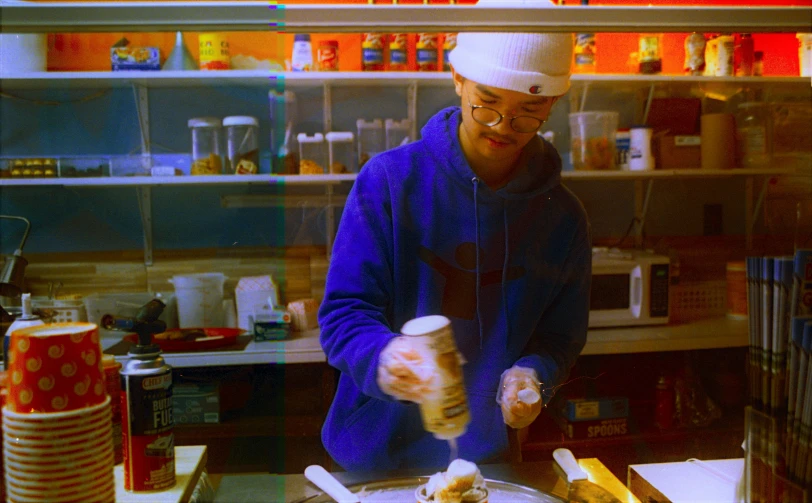 a man in a blue sweatshirt standing over a pizza on top of a table