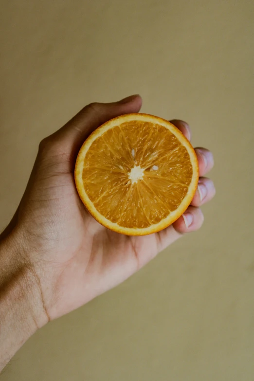 a hand holding an orange slice over a beige wall