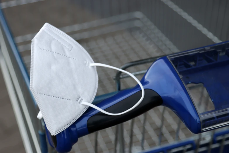 a white face mask with a blue handle sits on the handle of a shopping cart