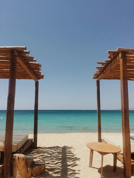 two wooden benches sitting in the sand near the ocean