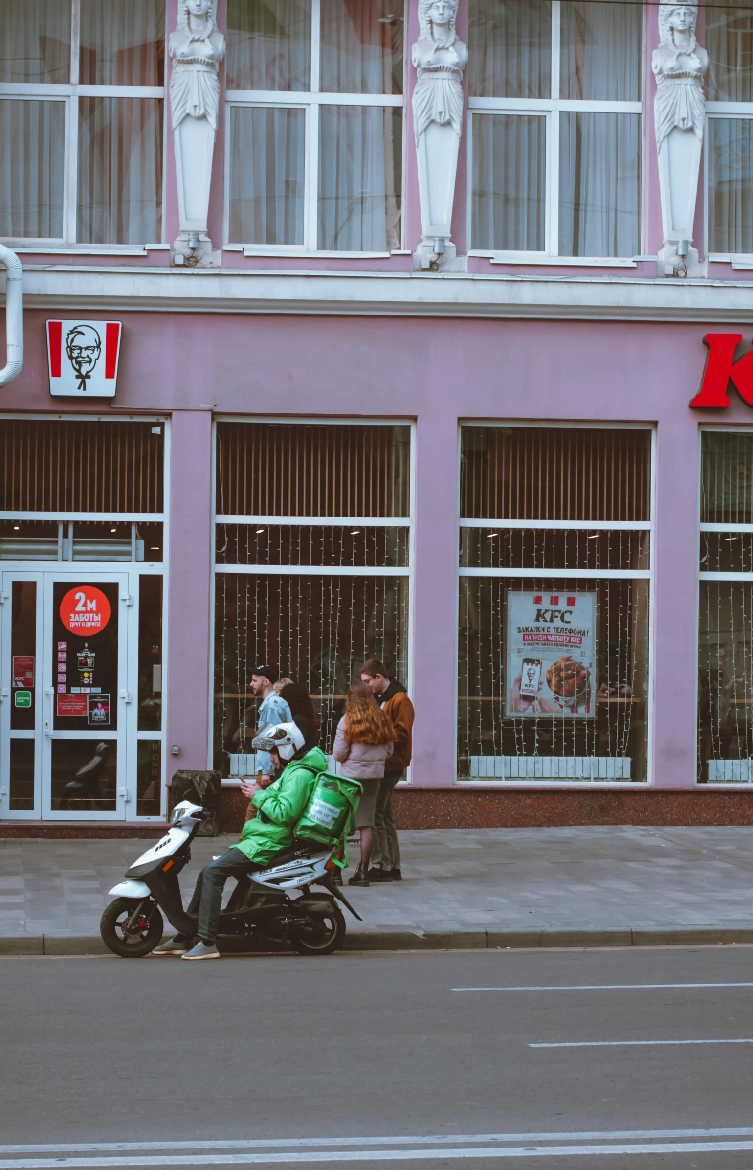 a woman with green pants and a man sit on a motorcycle