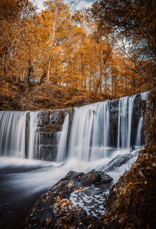 the river runs beneath a waterfall in autumn