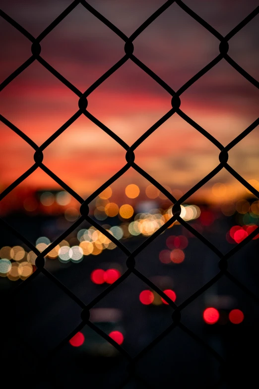 the lights from the cars are shown through the chain link fence