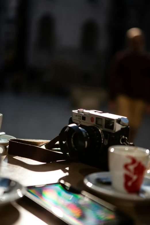 a camera sits on a table with tea cups and saucers