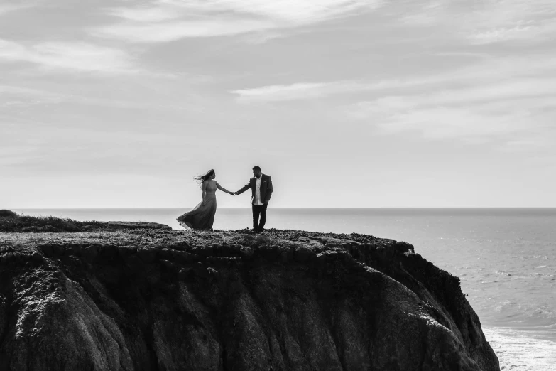 a man and woman on a rocky outcropping overlooking the ocean