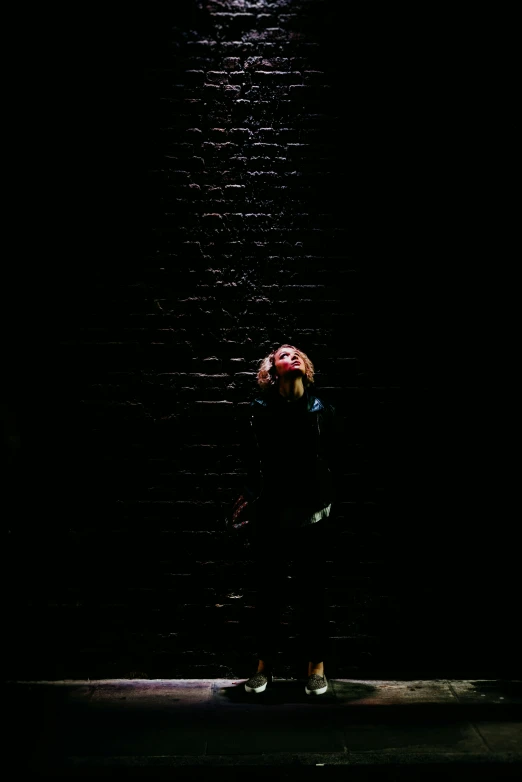 a woman standing on the sidewalk in the dark under an umbrella
