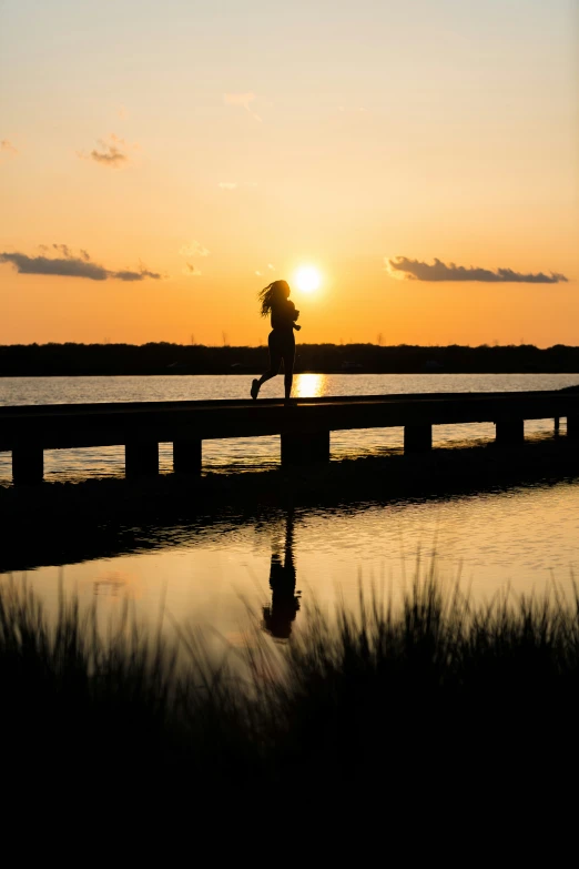 the sun rises as a woman walks across the pier