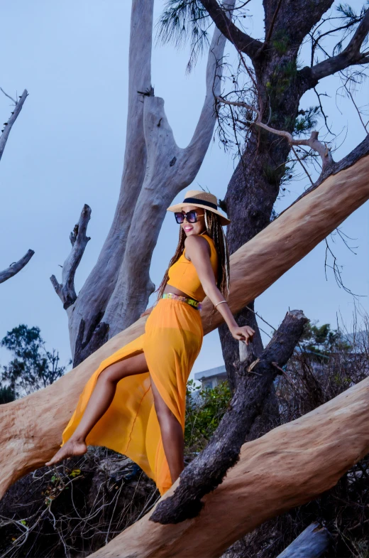 a woman wearing a yellow dress is posing in a tree