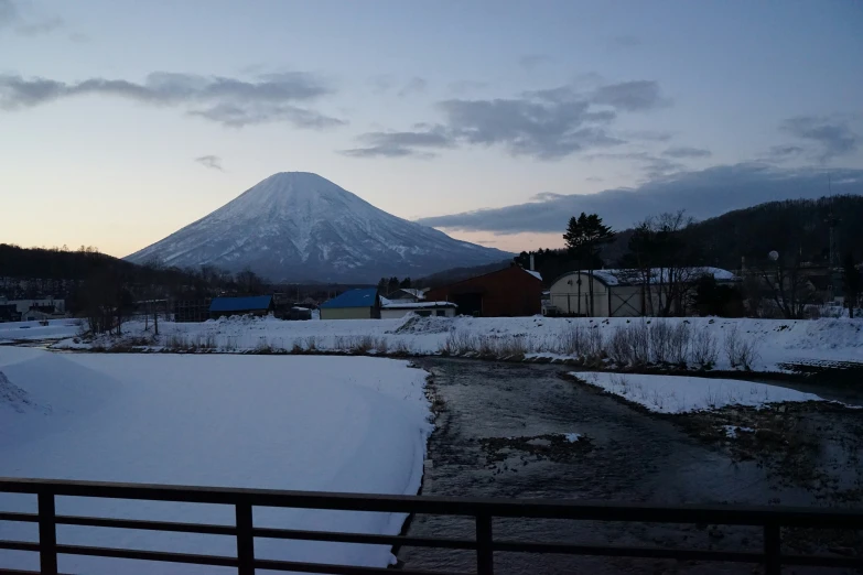 a snowy field with trees, buildings and a mountain in the background