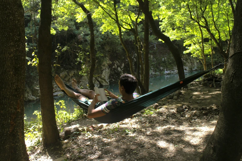 a young man sitting in a hammock reading