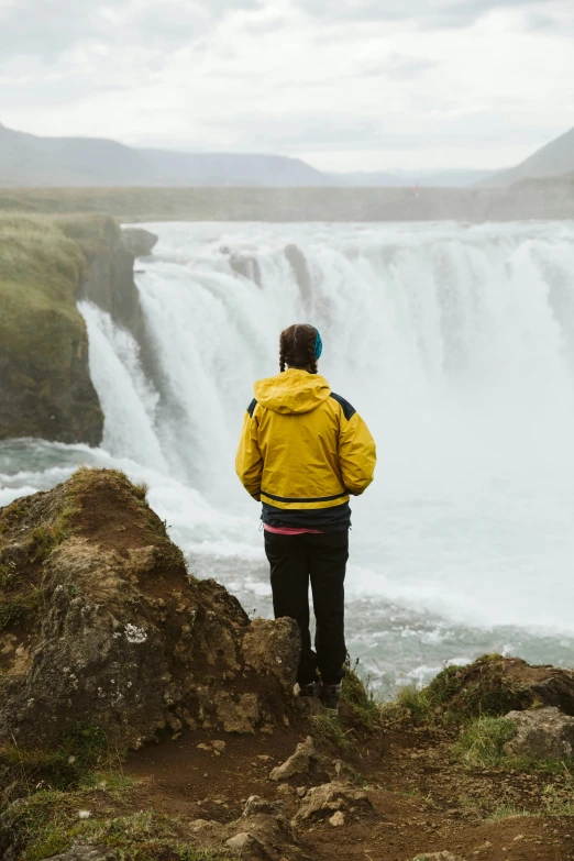 a person wearing a yellow jacket stands on rocks near a waterfall