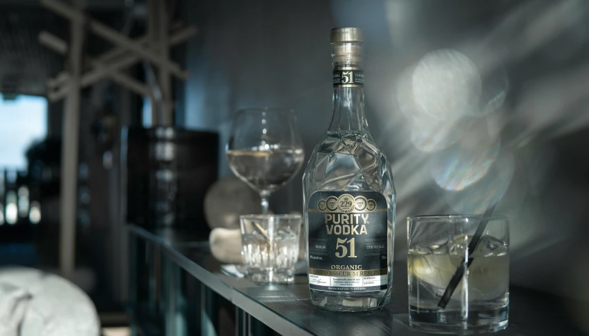 a bottle of whisky, glasses and plate of food sit on a shelf